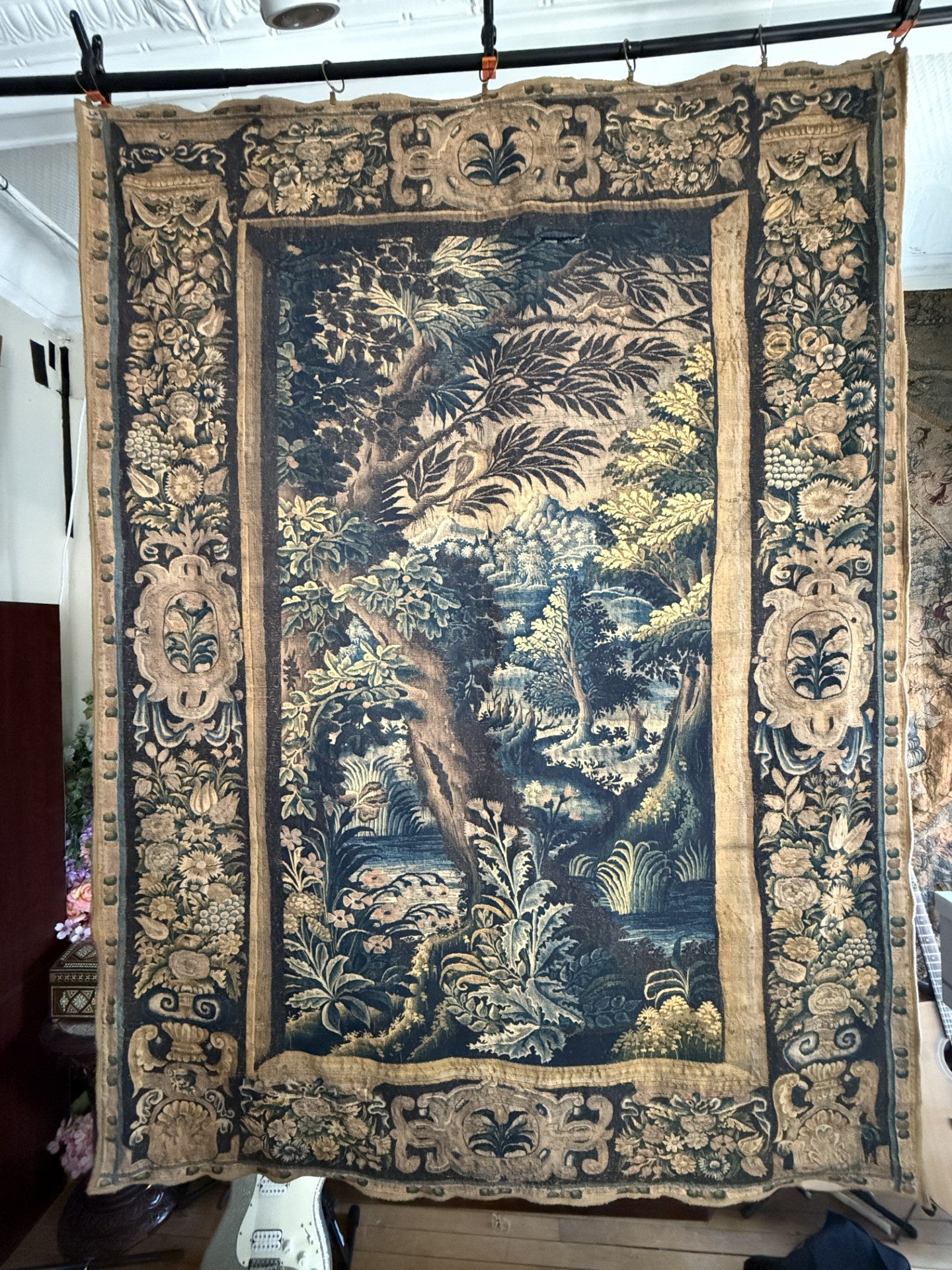 Decorative tapestry with intricate patterns and a natural scene, hanging on a rack.