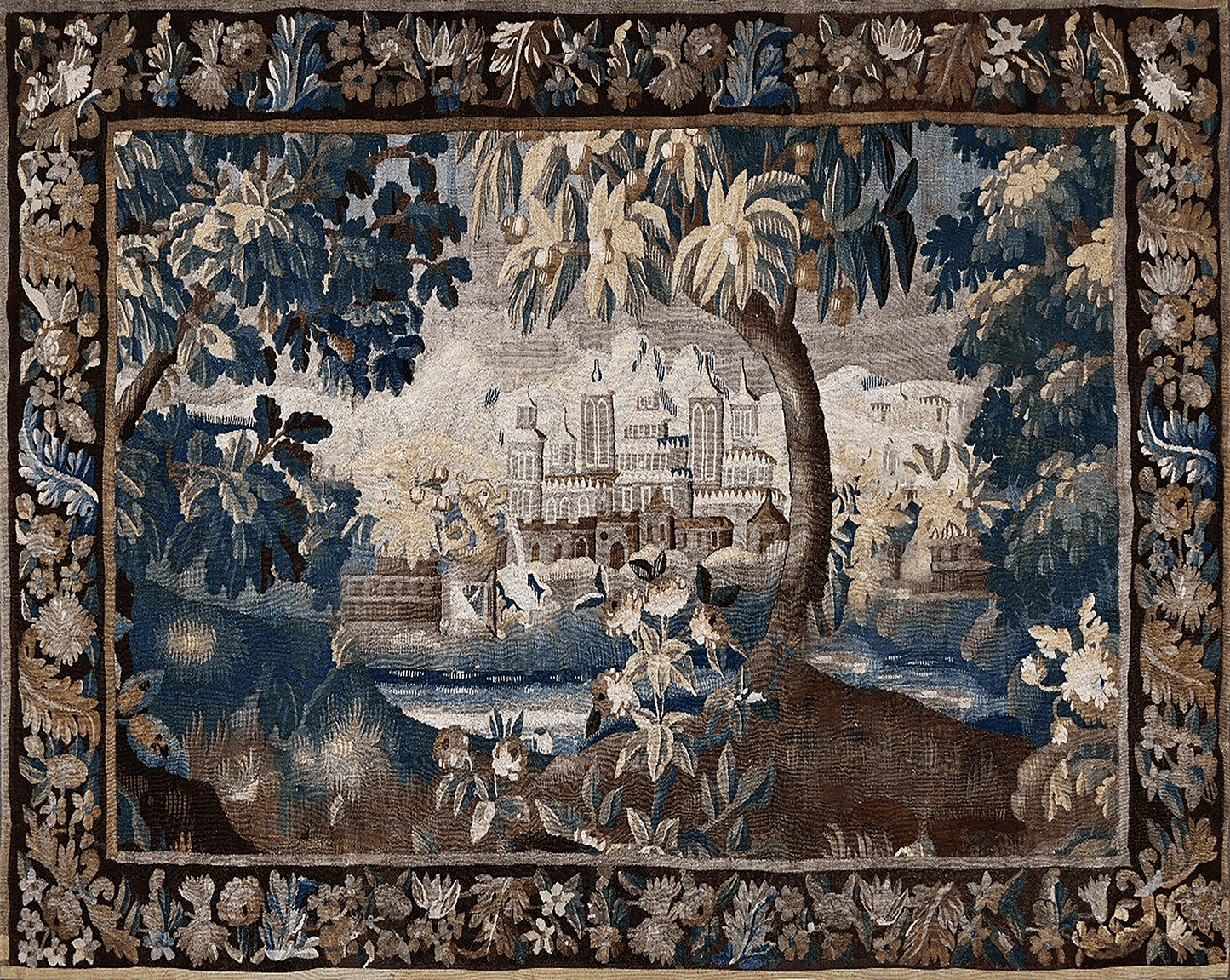 An ornate rectangular tapestry featuring a detailed landscape scene with a grand chateau, trees, water, and figures in the foreground, surrounded by a decorative floral border.