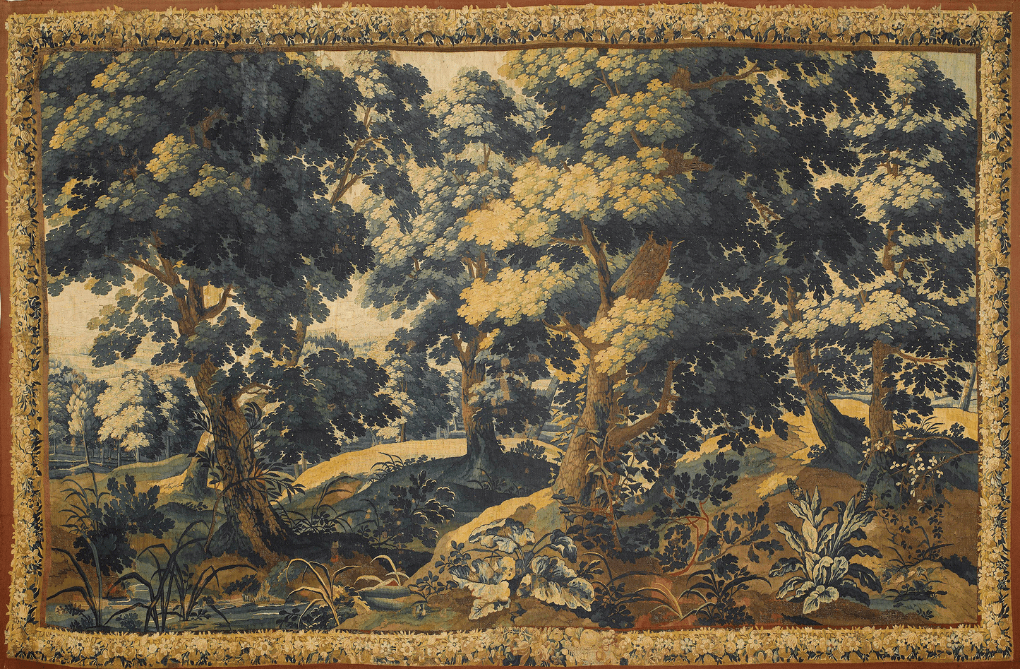 The image depicts a verdure tapestry, a genre of tapestry that flourished in the 16th and 17th centuries characterized by its focus on woodland landscapes and plant life. At first glance, you are drawn into a rich and dense forest scene, the textures and hues of green ranging from deep emeralds to light, almost golden shades, suggesting the interplay of sunlight filtering through the canopy above.