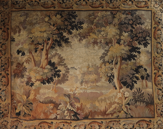 A 17th Century Flemish tapestry featuring a pastoral landscape with trees and a castle in the background, bordered by a floral pattern.