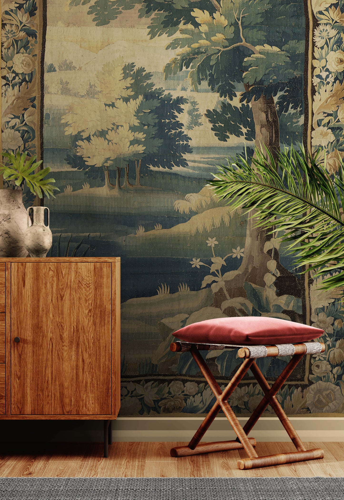 A styled interior scene featuring a large tapestry with a classical landscape scene of trees and water, mounted on a wall behind a wooden cabinet and a folding stool with a pink cushion.