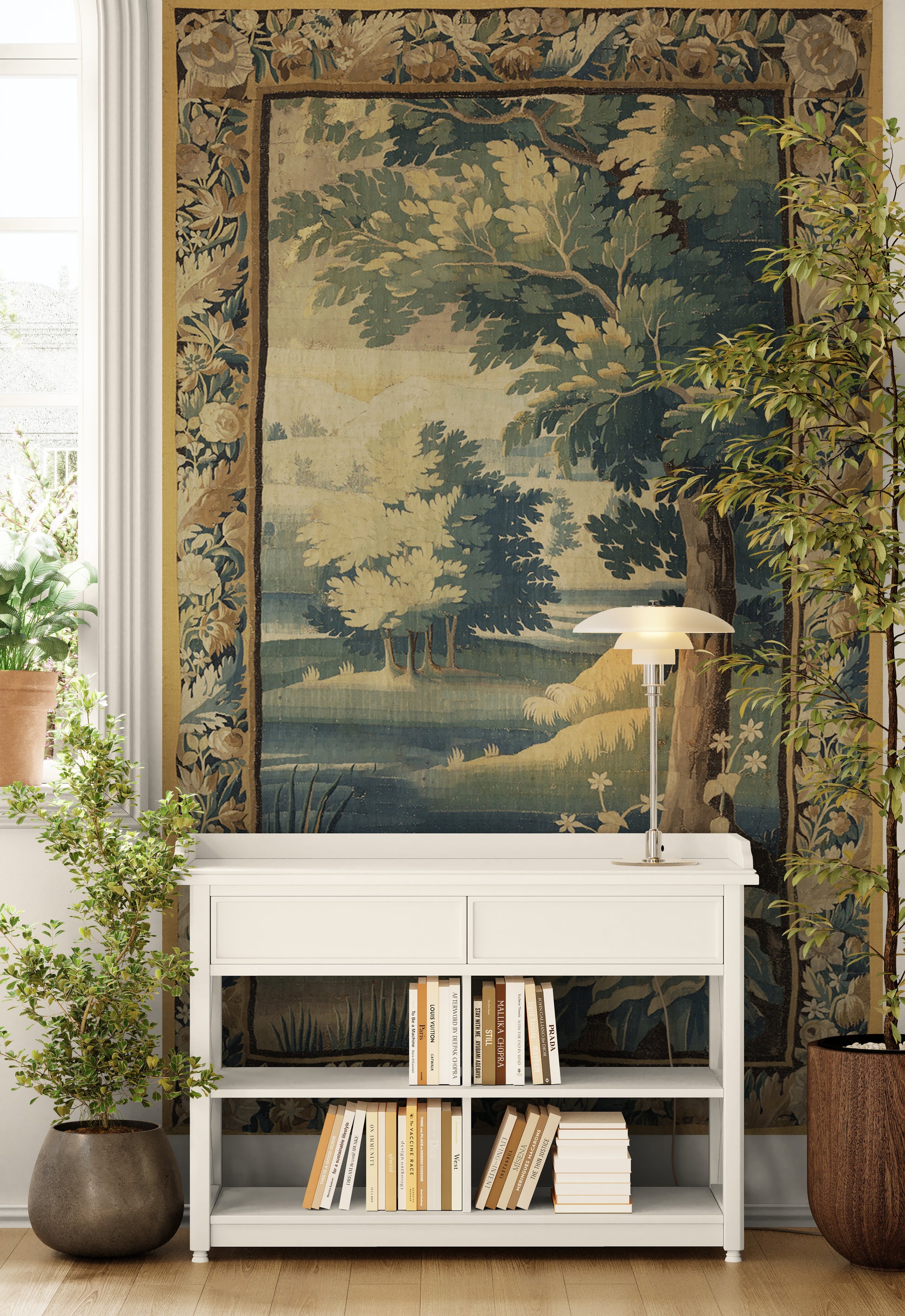 A large tapestry featuring a detailed landscape scene with trees and a river, styled in a room above a white console table with books and a lamp.