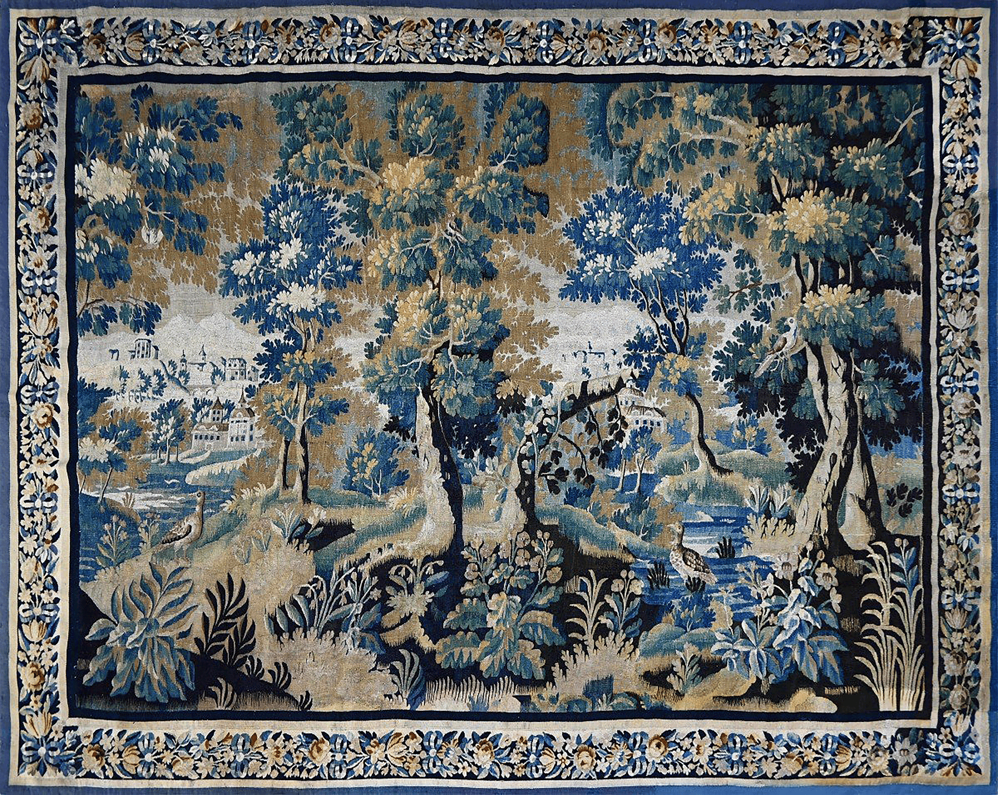 A square tapestry featuring a detailed landscape scene with blue and green trees, foliage, and a river, framed by an ornate floral border in blue, beige, and gold.