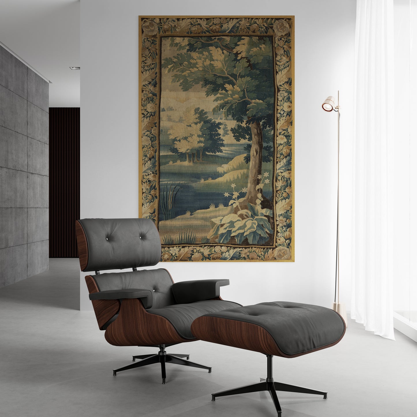 A classic Eames-style lounge chair with an ottoman in dark gray leather and walnut wood, positioned in a modern minimalist room below a large framed landscape tapestry.