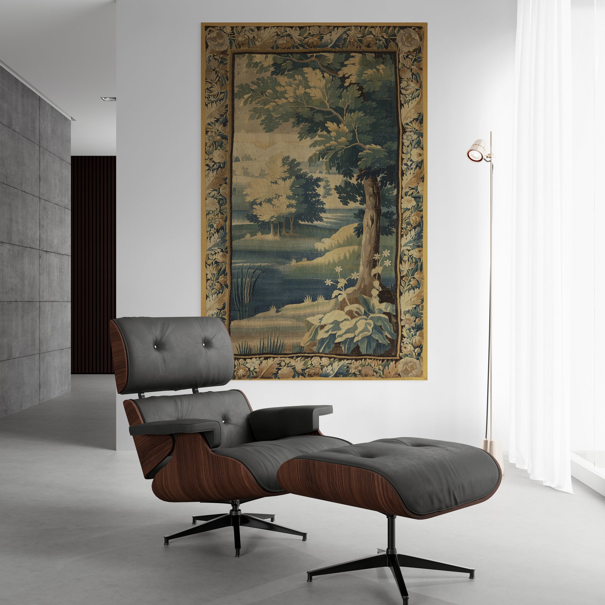 A classic Eames-style lounge chair with an ottoman in dark gray leather and walnut wood, positioned in a modern minimalist room below a large framed landscape tapestry.