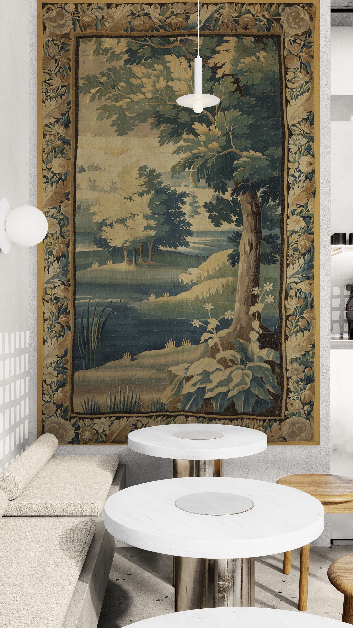 A large vintage-style landscape tapestry featuring a tree by a river, hung on a wall in a modern living room setting with white tables and a sofa.